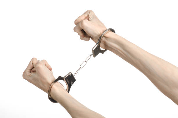 istock Prison and convicted topic: man hands with handcuffs isolated on white background in studio, put handcuffs on killer 1045448898