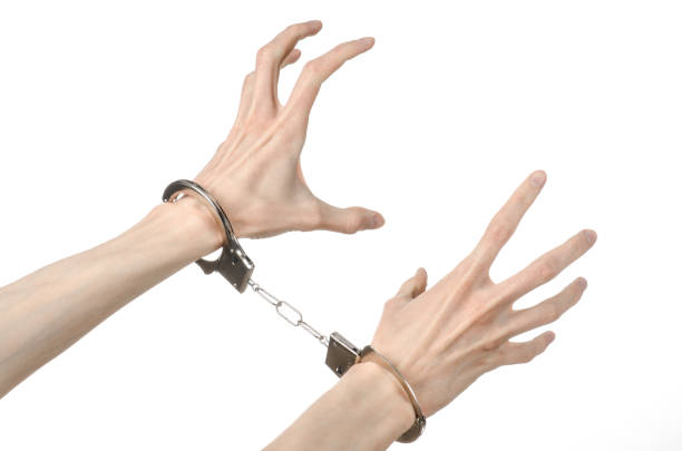 istock Prison and convicted topic: man hands with handcuffs isolated on white background in studio, put handcuffs on killer 1045451374