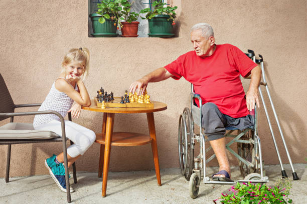 senior disabile e sua nipote che giocano a scacchi - senior adult wheelchair community family foto e immagini stock