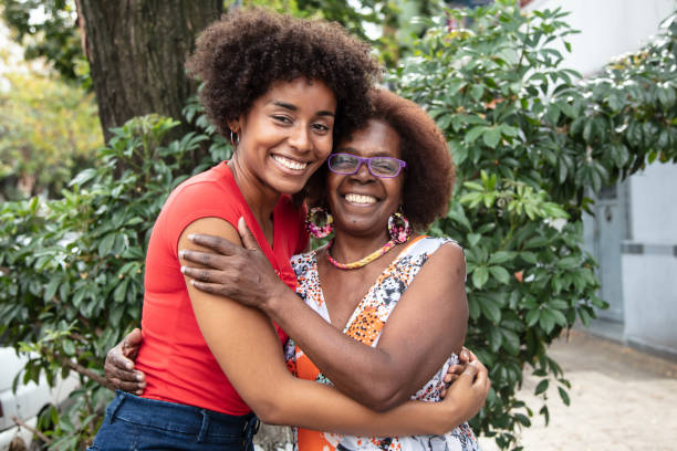 Portrait of beautiful mother and daughter embracing each other while looking at camera with a toothy smile Portrait of beautiful mother and daughter embracing each other while looking at camera with a toothy smile very happy black mother and adult daughter stock pictures, royalty-free photos & images