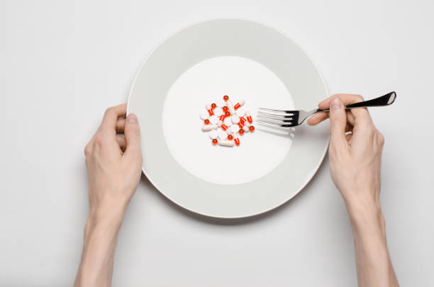 istock Medications and improper nutrition topic: human hand hold a plate with pills isolated on white background top view 1045466204