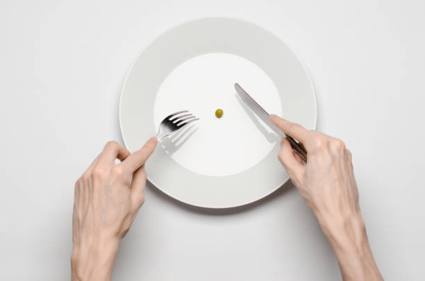 istock Healthy food theme: hands holding knife and fork on a plate with green peas on a white table top view 1045466586