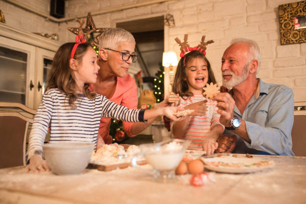 Grandparents and young girls holding Christmas cookies Senior couple making Christmas cookies for their beautiful two granddaughters multi generation family christmas stock pictures, royalty-free photos & images
