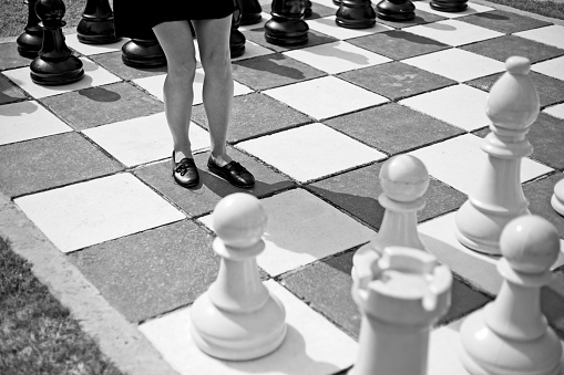 A Caucasian women standing in the middle of a large chess set.