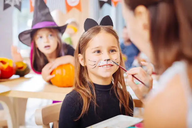 Extremely excited. Dark-eyed girl wearing cat Halloween costume feeling extremely excited celebrating in kindergarten