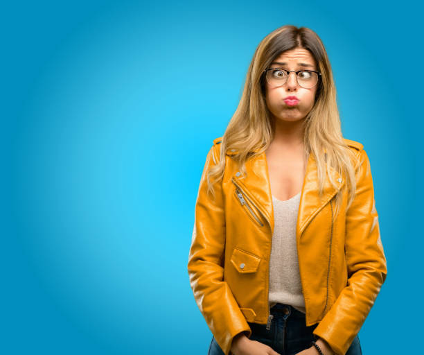 puffing out cheeks, having fun making funny face Beautiful young woman puffing out cheeks, having fun making funny face, blue background puffed up cheeks stock pictures, royalty-free photos & images