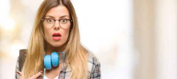 istock Young student woman with headphones and backpack happy and surprised cheering expressing wow gesture, pointing with finger 1045515212