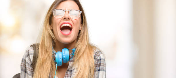 istock Young student woman with headphones and backpack stressful, terrified in panic, shouting exasperated and frustrated. Unpleasant gesture. Annoying work drives me crazy 1045515242