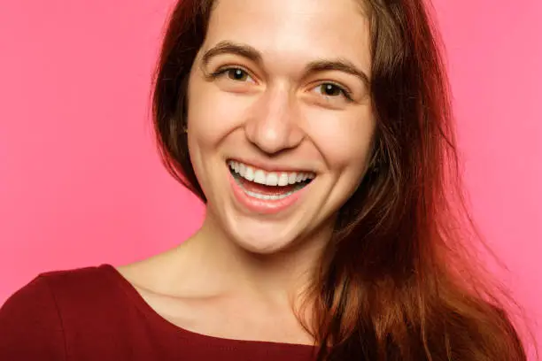 emotion face. very happy joyful thrilled to bits woman with beaming smile. young beautiful brown haired girl portrait on pink background.