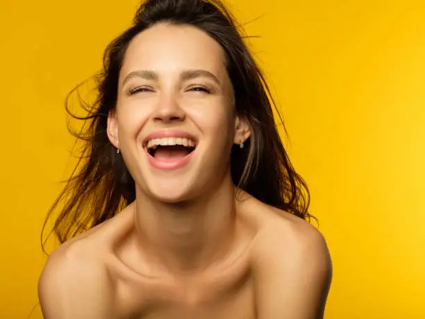 emotion face. very happy joyful thrilled to bits woman with beaming smile. young beautiful brown haired girl portrait on yellow background.
