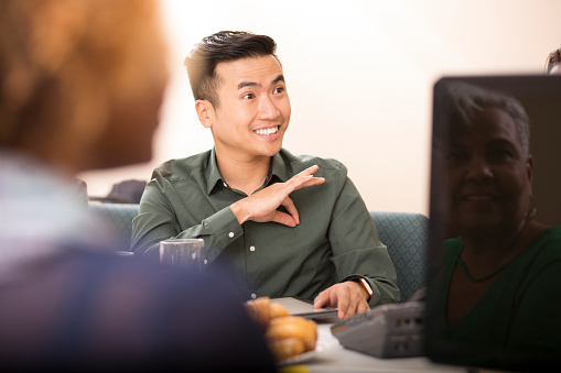 Multi-ethnic group of business people in team meeting.  Hearing impaired business man uses sign language to speak with interpreter during business presentation.