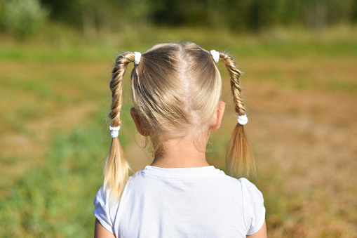 Little girl in white dress looks forward in the field, rear view, closeup