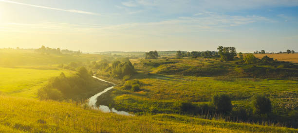 istock Sunny summer landscape with river flowing between the beautiful green hills,fields and meadows. 1045547600