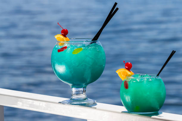 blue cocktail served in a fish bowl served on a railing with a natural water background as a travel concept