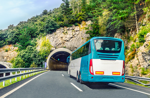 A white and blue coach, or long haul bus for tourists drives through the mountain tunnels and roads of Northern Spain, Europe on a summer day.
