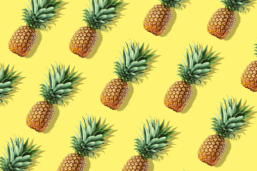 Colorful fruit pattern of fresh whole pineapples on yellow background