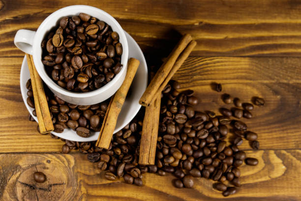 istock Coffee beans in white cup and cinnamon sticks on wooden table. Top view 1045603334