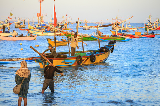 BALI, INDONESIA - AUGUST 7, 2017 : Asian fisherman on colorful handcrafted Balinese fishing boat at port in Jimbaran beach, Bali