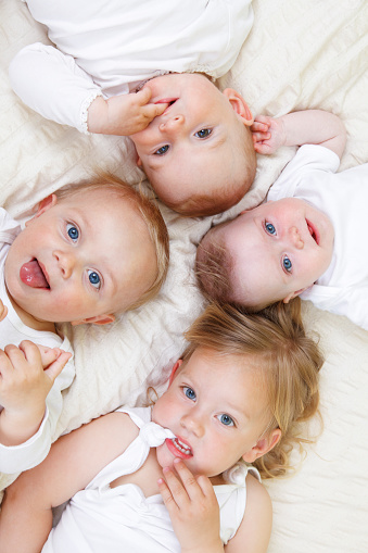 Four small children lying on a bed. Blue eyes, blond hair, white dress.