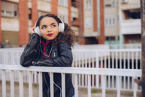 Mixed-race teen girl listens to music. Headphones, smart phone downtown.
