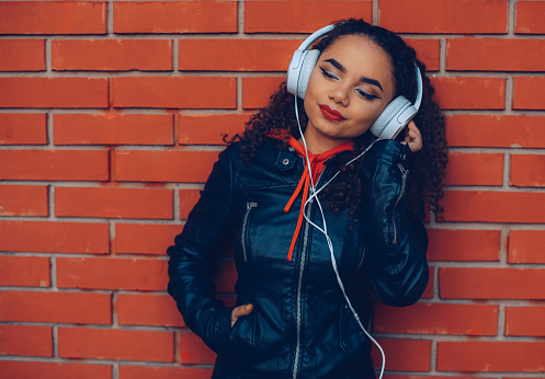 Mixed-race teen girl listens to music. Headphones, smart phone downtown.