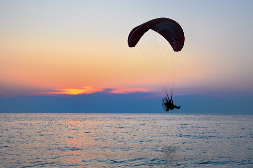A man is doing paragliding on the mediterranean sea at sunset