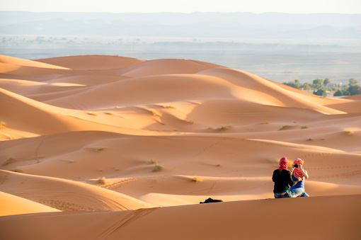 A couple is taking photos and selfies on the dunes of the Sahara Desert in Morocco. Merzouga is a small village in southeastern Morocco, about 35 kilometres southeast of Rissani. It is one of the most famous tourist destinations in Morocco.