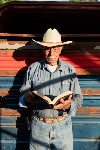 A senior mexican man standing and reading a Bible.