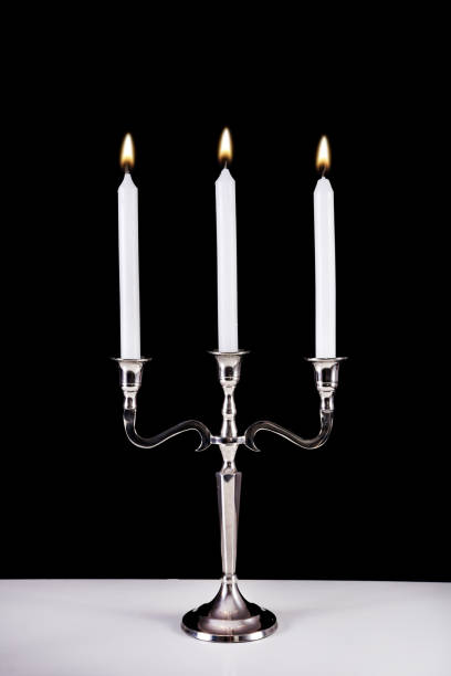 istock Silver baroque candlestick with three white paraffin candle burning on desk and black background 1045671548