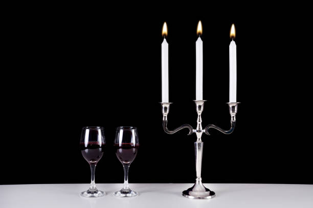 Beautiful old baroque candlestick and two red wine glasses on white table and black background. Romantic diner concept. Space for design and text. Retro and vintage background.