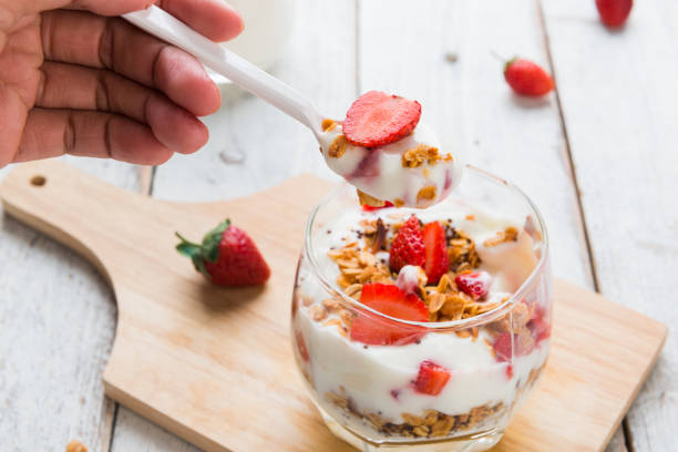 Strawberry , granola and yogurt healthy breakfast parfait on wooden background with hand and spoon