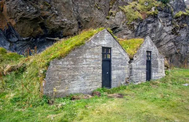 Two old turf-roofed houses near a rock cliff in Iceland.
