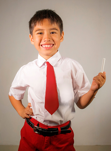 isolated portrait of 7 or 8 years old young happy and excited schoolboy in school uniform holding chalk smiling cheerful enjoying the back to school in child education concept