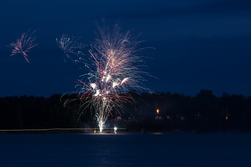 Fireworks display over a lake in northern Minnesota.  Campground with trees,campers, boats and unrecognizable people on the far lakeshore.
