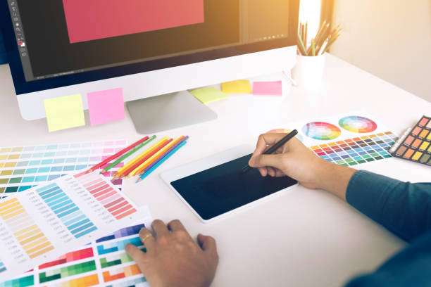 istock Freelance creative designers working on desk using digital graphic tablet and drawing with pen in modern home office. 1045747100