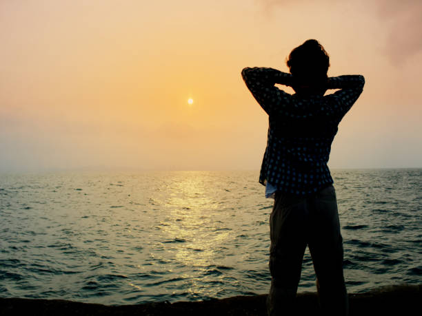 istock Back view of relaxed young Asian man standing with sunset background. 1045767440