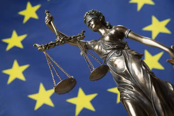 Statue of the blindfolded goddess of justice Themis or Justitia, against an European flag, as a legal concept