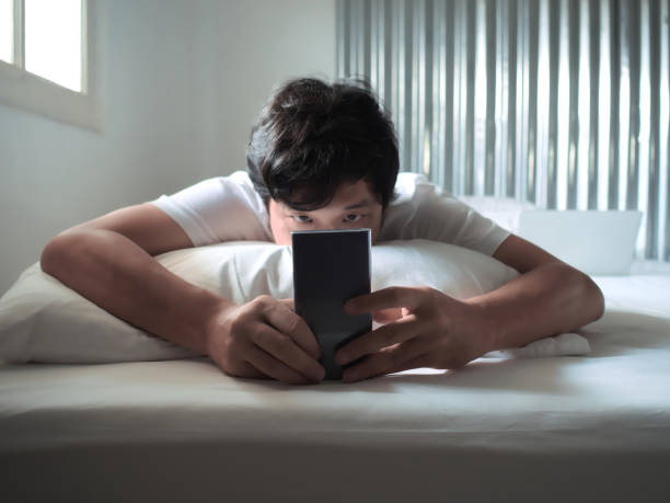 istock Relaxed Asian man with mobile smart phone lying down on the bed in morning 1045768140