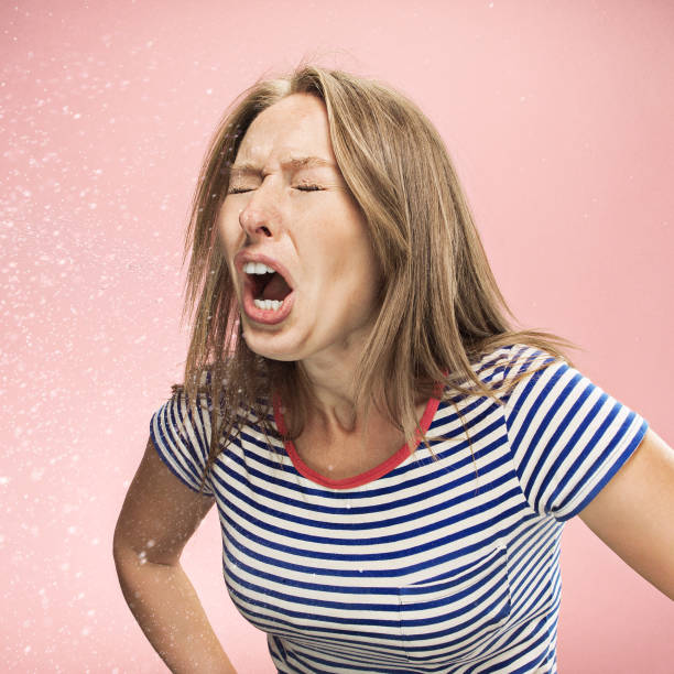 Young woman sneezing, studio portrait Young funny woman sneezing with spray and small drops, studio portrait on pink background. Comic, caricature, humor. illness, infection, ache. Health concept sneezing photos stock pictures, royalty-free photos & images