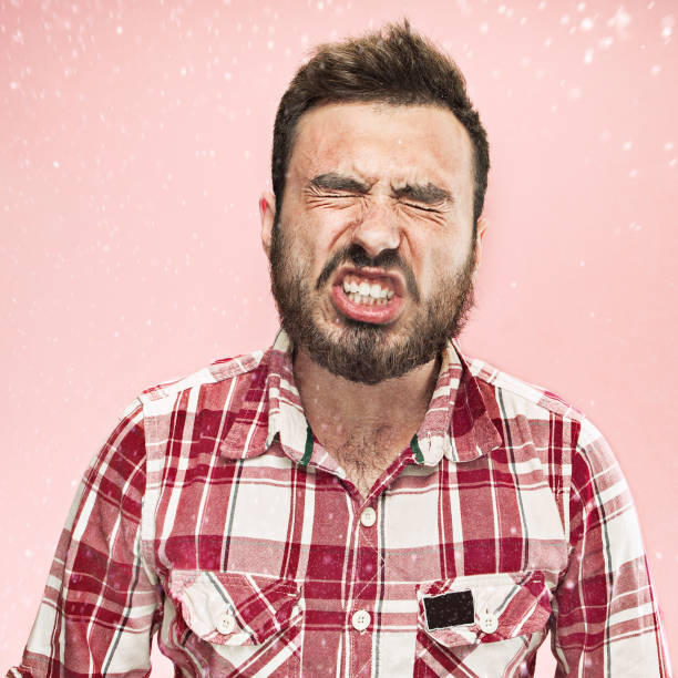 Young funny handsome man with beard and mustache sneezing with spray and small drops, studio portrait on pink background. Comic, caricature, humor. illness, infection, ache. Health concept