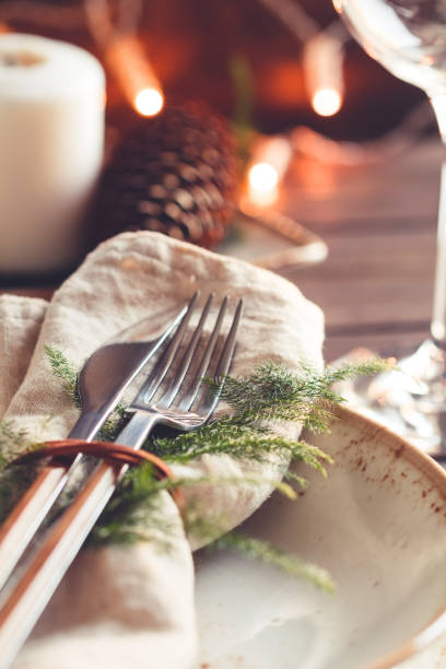 istock Thanksgiving table setting among white candles and cones. Ceramic plate with fork and knife on a linen napkin. Close up. 1045833240