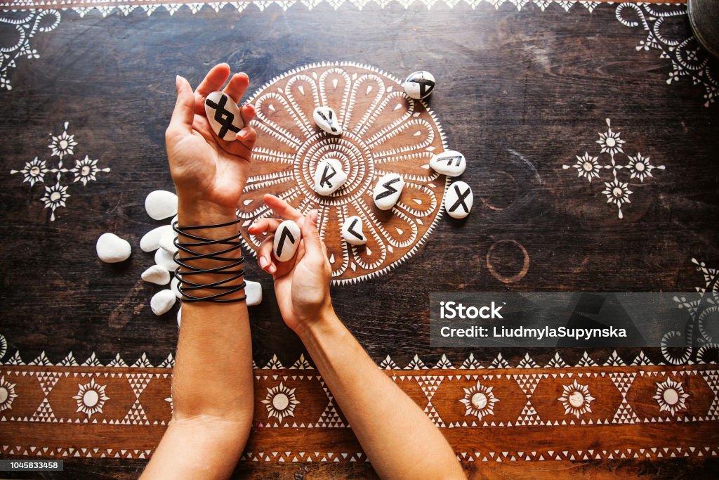 Runes hands holding runes stones on an ornate table Runes Stock Photo