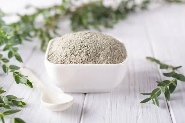 Photo of Ceramic bowl with green clay powder and fresh eucalyptus leaves on white background. Concept of face and body care.