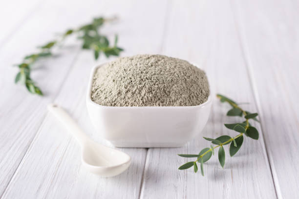 istock Ceramic bowl with green clay powder and fresh eucalyptus leaves on white background. Concept of face and body care. 1045842284