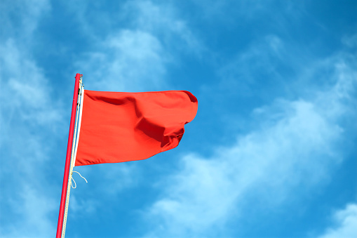 big red flag waving in the wind with the background of the blue sky and some clouds