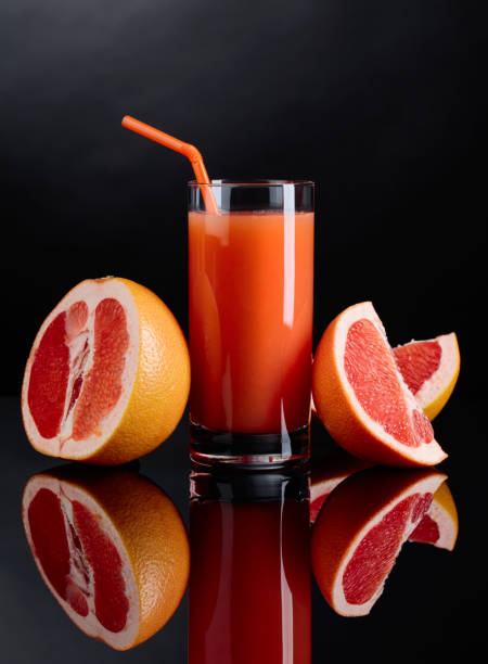Glass of  grapefruit juice and cut fruits on black background.