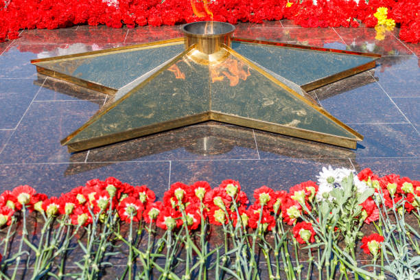 istock Many red flowers lie on a black granite monument with a star from which a orange fire burns. 1045850218