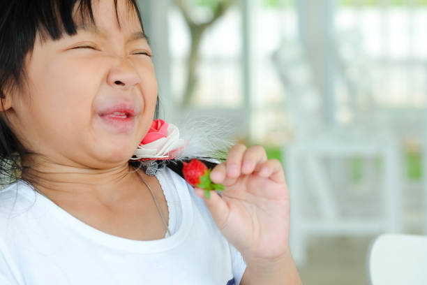 ładna azjatycka dziewczynka jedząca truskawkę, twarz pokaż kwaśną - lemon sour taste biting eating zdjęcia i obrazy z banku zdjęć