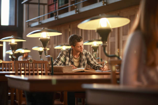 istock Young man reading a book in public library 1045865670