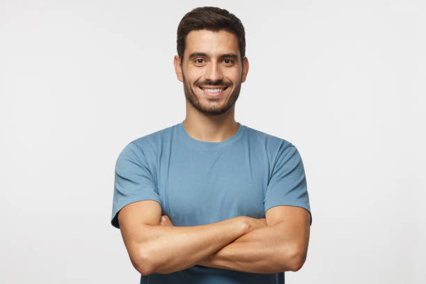 porträt des lächelns gut aussehender mann in blauem t-shirt stand mit verschränkten armen auf grauem hintergrund isoliert - arm anatomiebegriff fotos stock-fotos und bilder